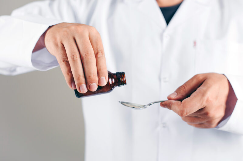 A doctor pouring syrup for someone on a gray background. side view.